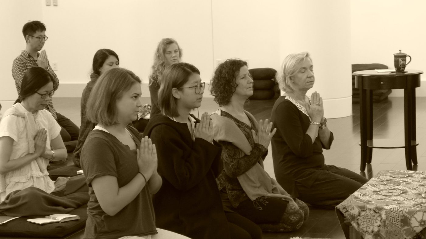 Practitioners with hands in prayer during a supplication practice
